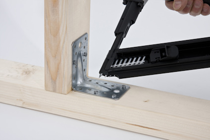 Hörn av träkonstruktion med metallbeslag; en spikpistol används för att fästa delarna.