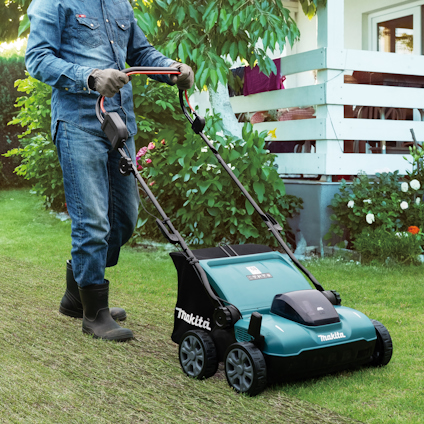 Person i jeanskläder klipper gräsmatta med en blå och svart gräsklippare från Makita.