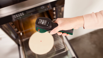 En person håller en infraröd termometer som visar 250 grader C framför en ugn med en pizzasten.