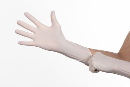 En person tar på sig vita latexhandskar.