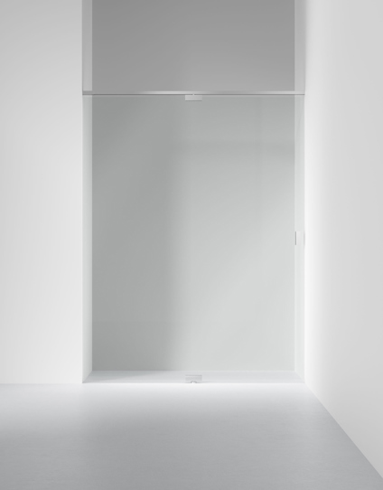 Glasvägg med metallram monterad mellan två vita väggar i ett minimalistiskt rum.