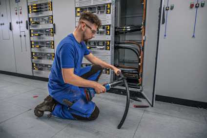 Person i blå arbetskläder arbetar med kabeldragning vid en elektrisk utrustning.