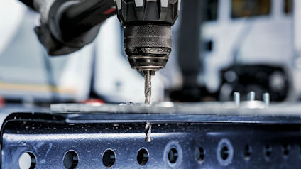 Borrmaskin borrar genom metallplåt som sitter på perforerat stålbord.