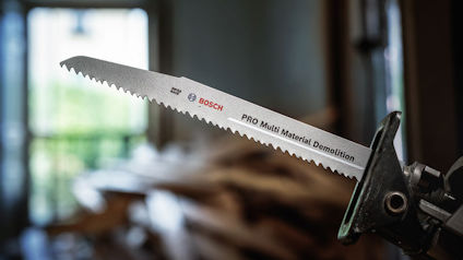 Sågblad märkt "Bosch PRO Multi Material Demolition" i en hållare, med suddig bakgrund av byggmaterial.