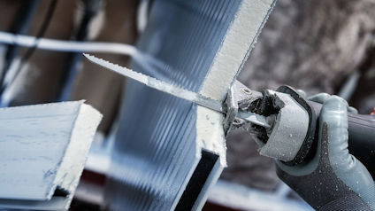 En person sågar genom en isolerplatta med en elektrisk såg.