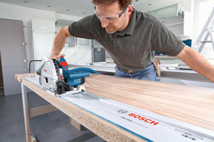 En person använder en cirkelsåg från Bosch för att skära en träplanka i ett modernt rum.