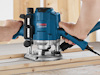 Två händer använder en blå Bosch Professional fräs på träplankor.