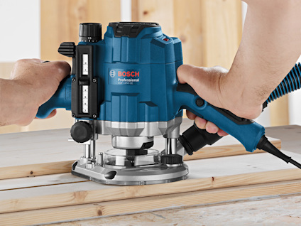 Två händer använder en blå Bosch Professional fräs på träplankor.