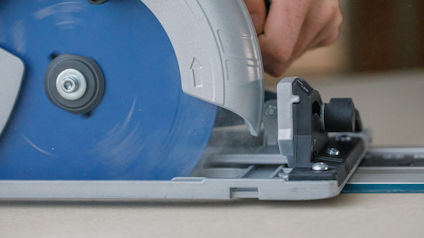 Cirkelsåg med blå klinga och silverfärgat hölje som skär genom material. En hand greppar verktyget.