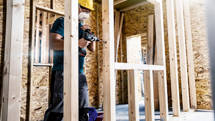 Person monterar träreglar i byggnad med osb-skivor, klädd i hjälm.