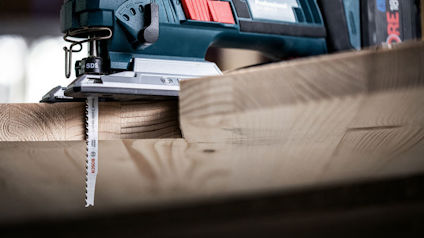 Sticksåg med sågblad skär genom träplanka.