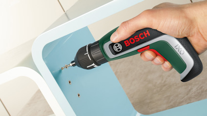Hand håller en Bosch-skruvdragare som skruvar i en blå yta.