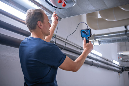 Person i mörk tröja inspekterar ventilationssystem med en kamera.