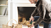 Man staplar trä i en korg framför en eldstad.