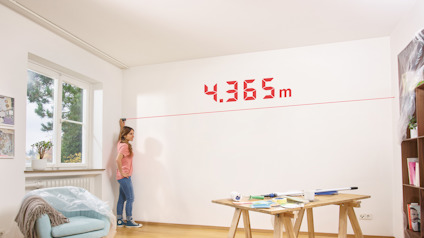 Kvinna i rosa tröja mäter en vägg med laserlinje och texten "4.365 m" synlig ovanför.