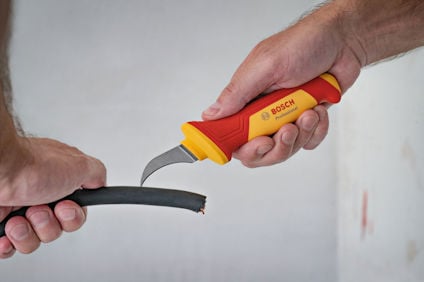 Två händer håller en kabelskalare med texten "BOSCH" och skalar en svart kabel.