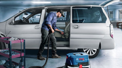 Person som rengör bilens insida med en dammsugare i ett garage.