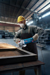 Person med skyddsutrustning slipar metall med vinkelslip i fabrik.