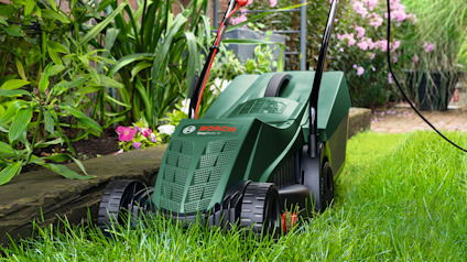Grön gräsklippare från Bosch på en gräsmatta, omgiven av trädgårdsgrönska och blommor.