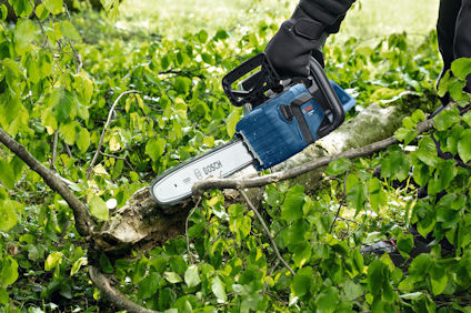 Person sågar en gren med en motorsåg i ett grönt buskage.