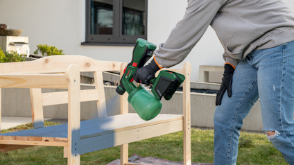 En person slipar en trämöbel med en grön slipmaskin utomhus.