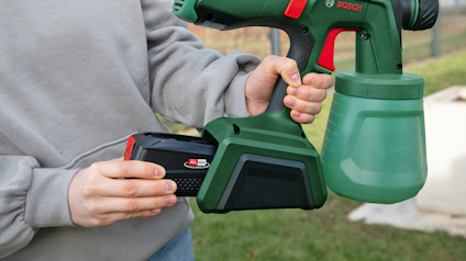 Person håller en grön och svart målningsspruta med ett rött och svart batteri.