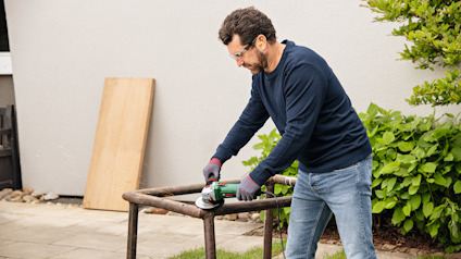 En person slipar ett metallrör utomhus med en vinkelslip.