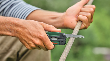 Person håller i ett verktyg med sågklinga och kapar en träpinne.