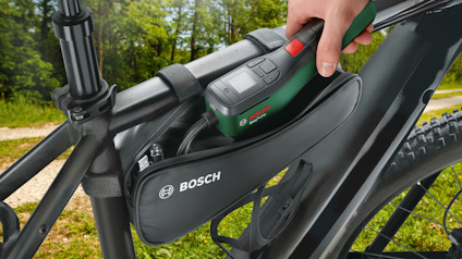 En mätanordning tas ut ur en Bosch-märkt väska på en cykel, i en skogsmiljö.
