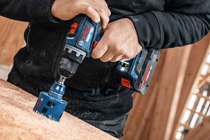 En person borrar i trä med en Bosch borrmaskin, använder ett stort sågblad.