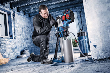 Person arbetar med en borrmaskin i ett industriellt utrymme, klädd i skyddande arbetskläder.