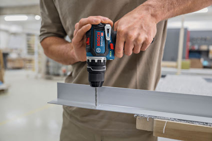 En person borrar i metall med en Bosch sladdlös borrmaskin inomhus.