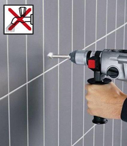 Hand som håller en borrmaskin mot kakelvägg, skylt med överkryssad borr och vatten.