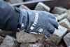 Hand med svart handske, märkt "TEGERA", håller en sten bland andra stenar. Handsken har ett snöflingemärke.