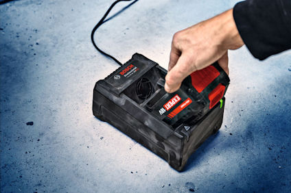Hand sätter Bosch-batteri i laddare på betonggolv.