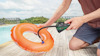 En person pumpar upp en orange simring med en svart slangpump vid en pool.