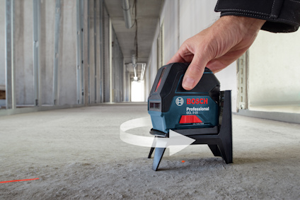 Hand justerar en Bosch Professional lasermätare som projicerar en röd linje på golvet i en byggnadskorridor.