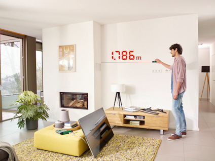 Person i ett vardagsrum mäter väggens längd med en digital mätare som visar 1,786 m.