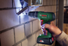 Hand håller en Bosch sladdlös borrmaskin mot en tegelvägg. Batteriindikatorn lyser grönt.