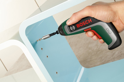 En hand håller i en grön och svart sladdlös skruvdragare med texten "BOSCH" i rött.