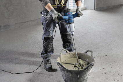 Person som använder en elektrisk mixer för att blanda cementmassa i en hink.