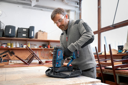 Man in workshop using a blue power tool at a wooden table.