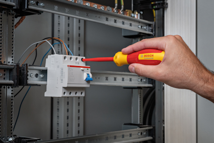Hand som använder en Bosch-skruvmejsel för att arbeta på en elektrisk brytare i ett elskåp.