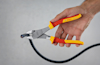 Händ klipper en svart kabel med en Bosch avbitartång med rött och gult handtag.