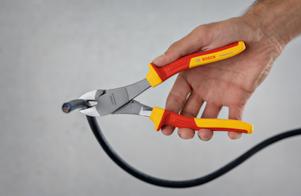Händ klipper en svart kabel med en Bosch avbitartång med rött och gult handtag.
