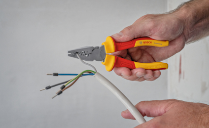 En person håller en tång och avmantlar en kabel med flerfärgade ledningar synliga. Tången är märkt "Bosch".