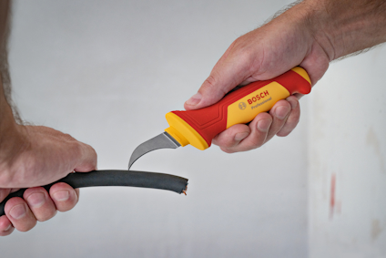 Hand som håller en Bosch-kniv och skär ett svart isolerat kabelrör.