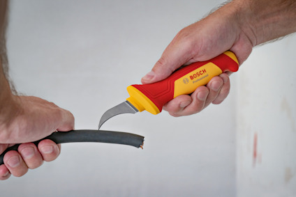 Två händer håller en kniv och en kabel. Kniven skär genom kabelns isolering.