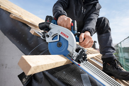 Person som använder en cirkelsåg från Bosch för att såga trä på ett byggarbetsplats.