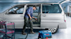 Man using a vacuum cleaner to clean the interior of a van in a garage setting.